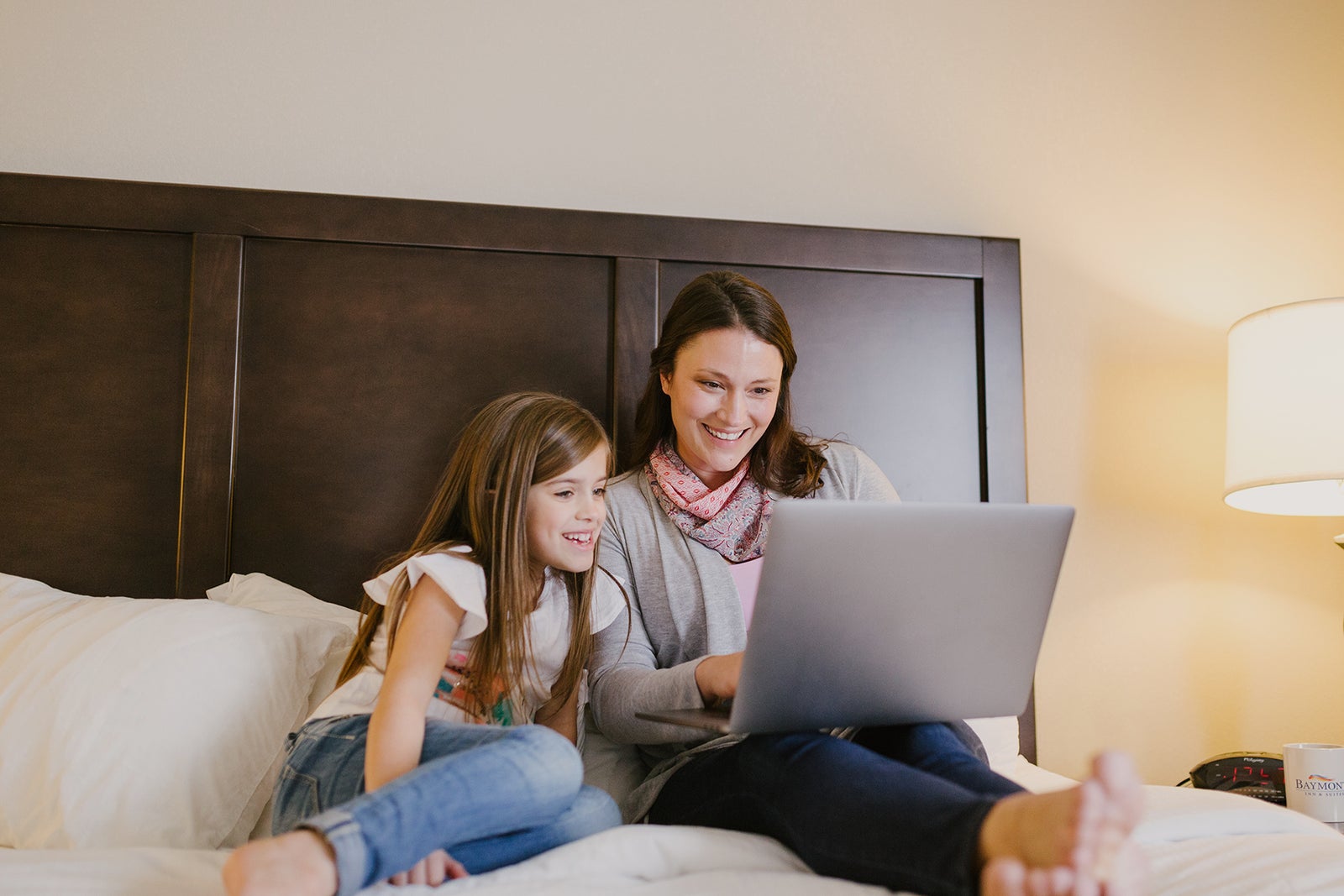 Woman and young girl smiling while using a laptop together on a bed.