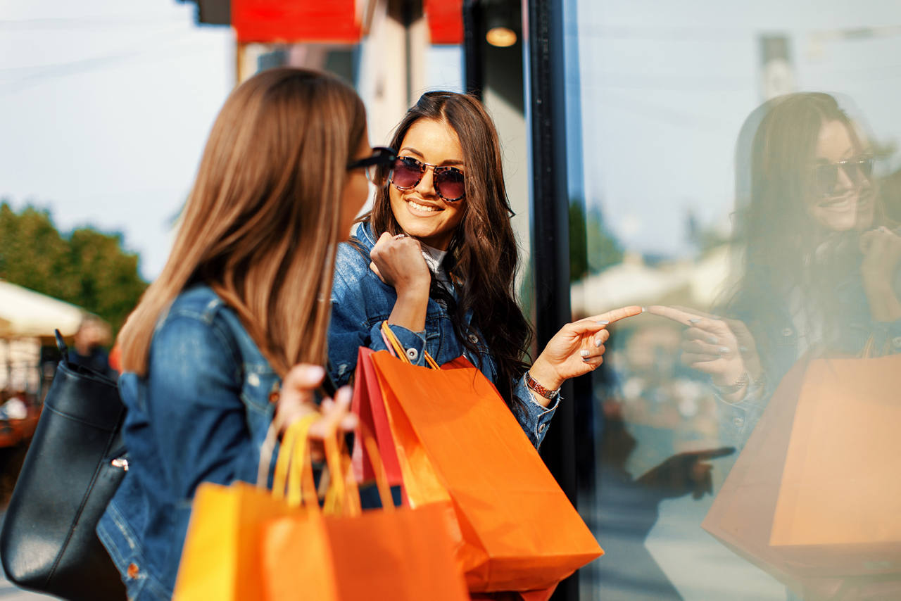 Twin women with matching packages standing in front of a store window. 