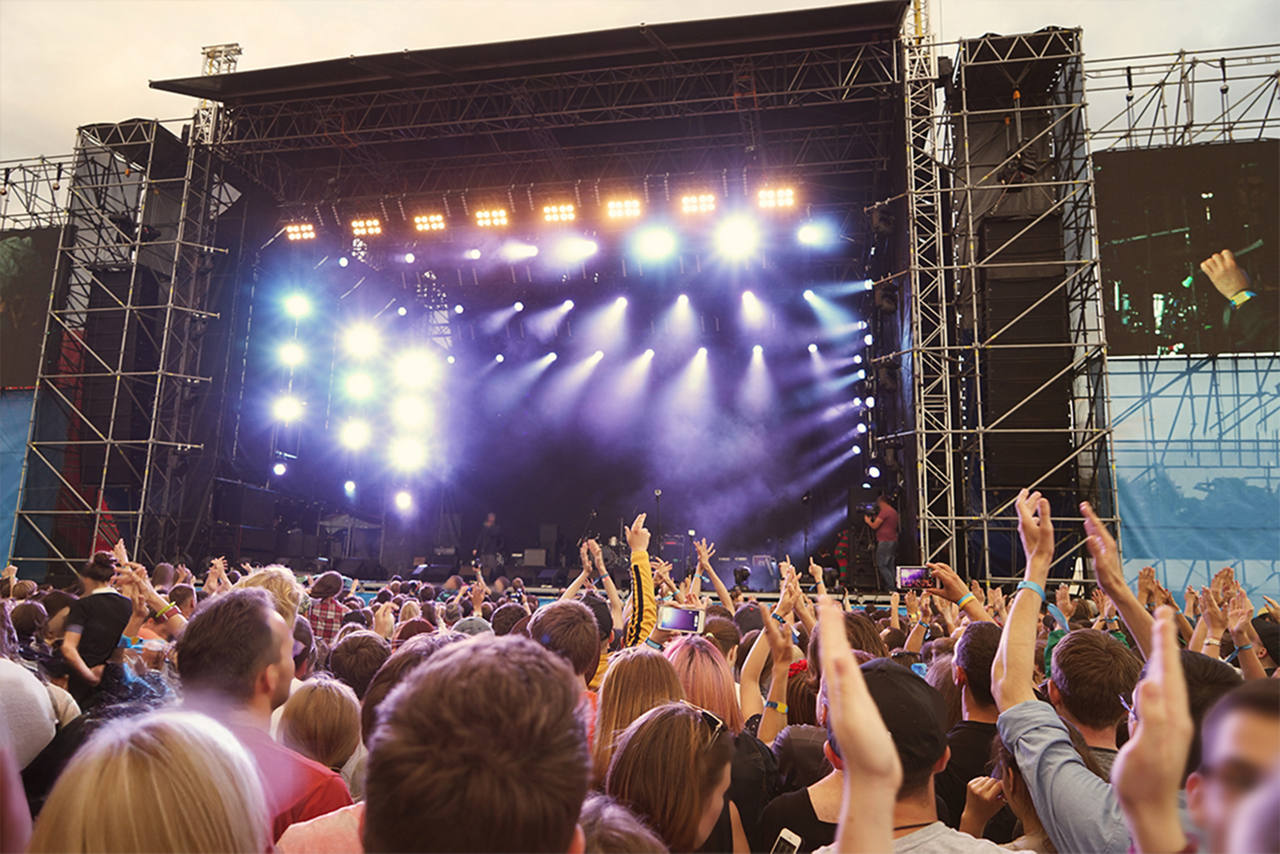 A lit concert stage with a packed audience watching the band on it.