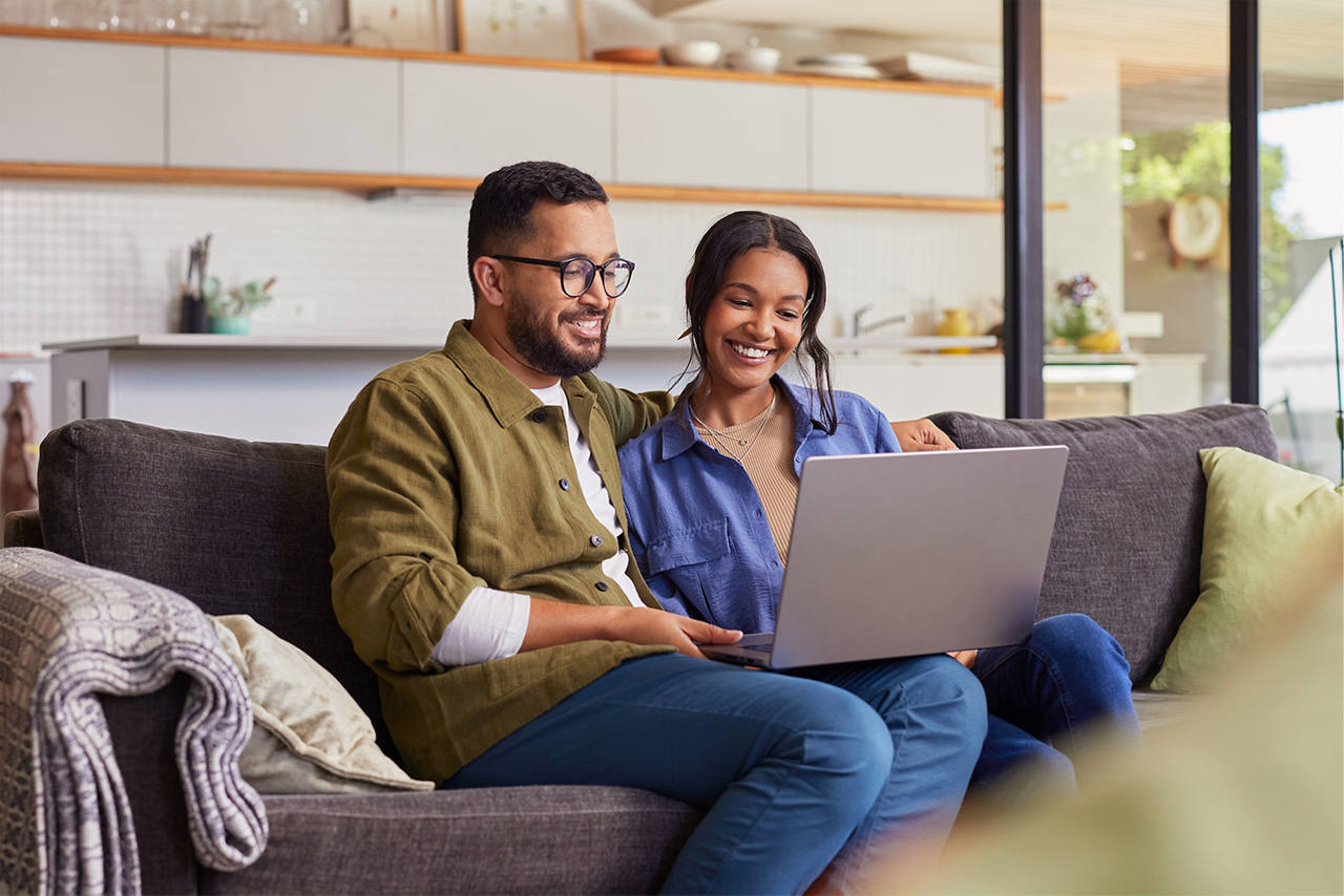 A couple on a comfortable couch, looking into a laptop together.