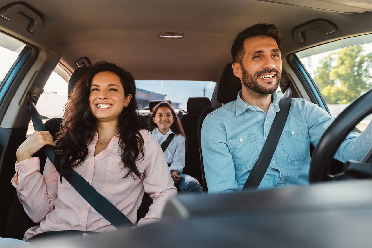A family of three in a car, smiling as they ride.